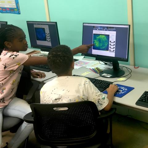 Two middle-school aged youth working at a computer screen with one of them pointing to an image of an astronomical object on the screen.