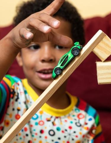 A child playing with a toy car on a ramp