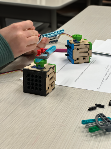 A student uses a smart motor, a small cube shaped device with a motor and a screen, on a desk.