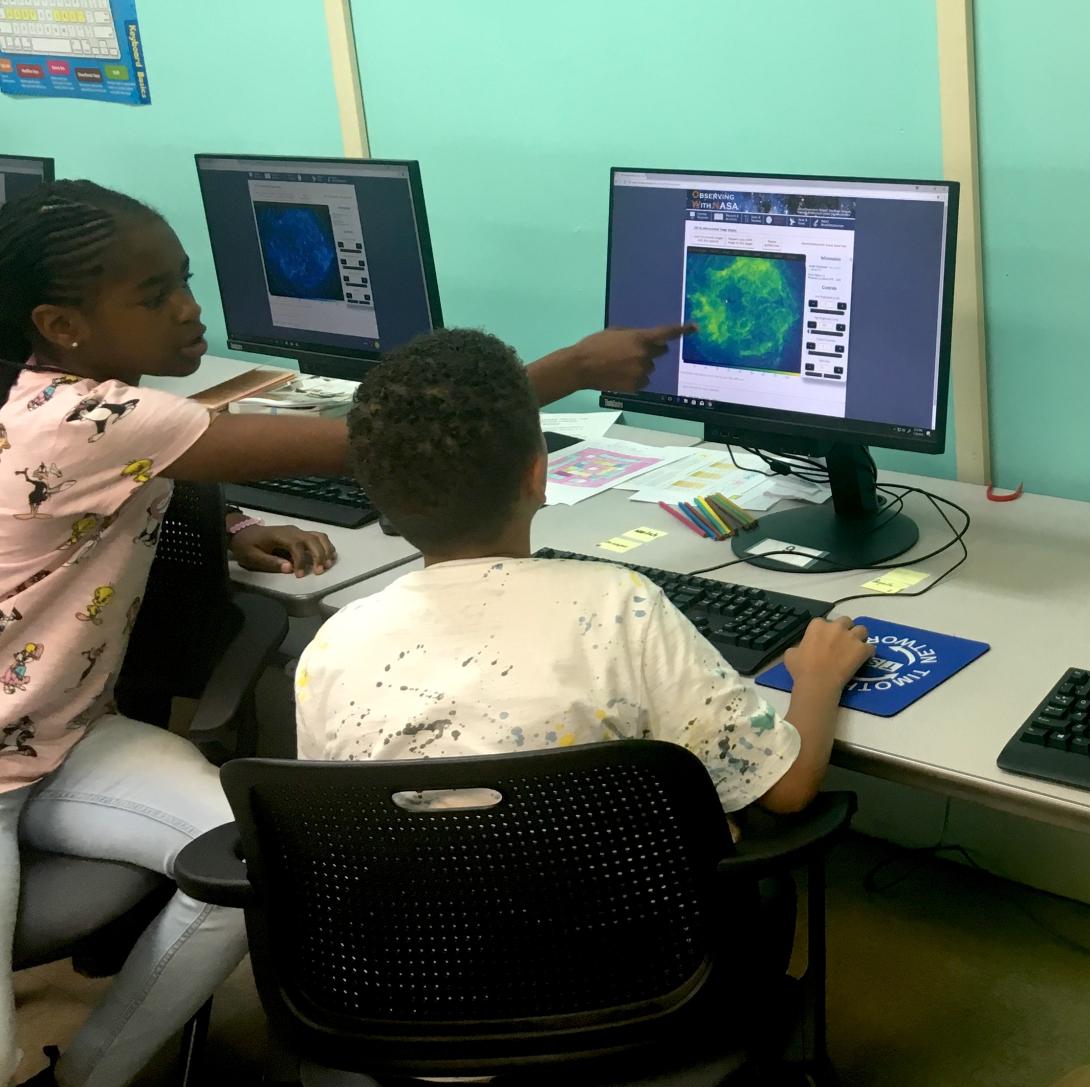 Two students working on computer with an astronomical image
